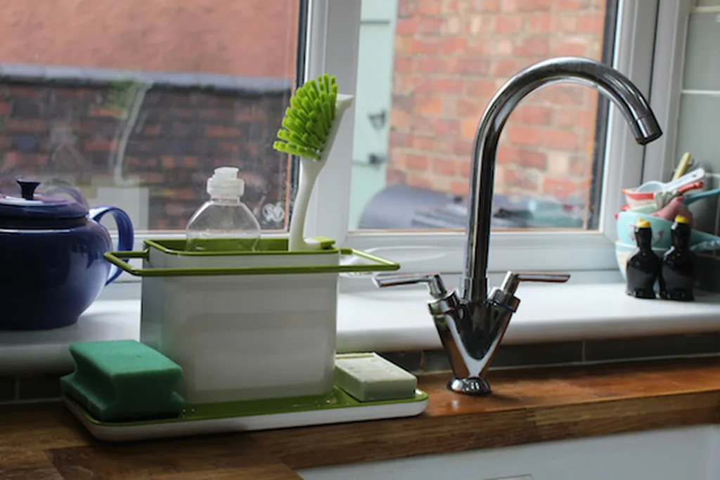 Kitchen sink below a window with washing up items kept on a small tray.