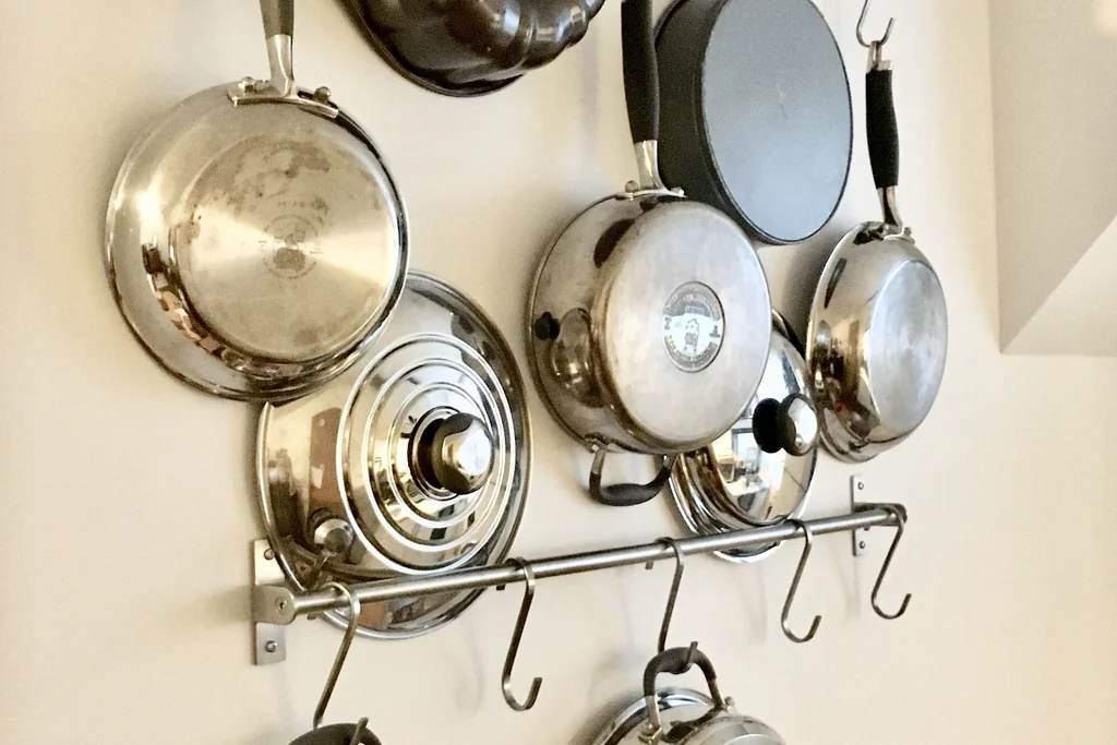 Pots and pans hanging from a black metal rail mounted on a kitchen wall.