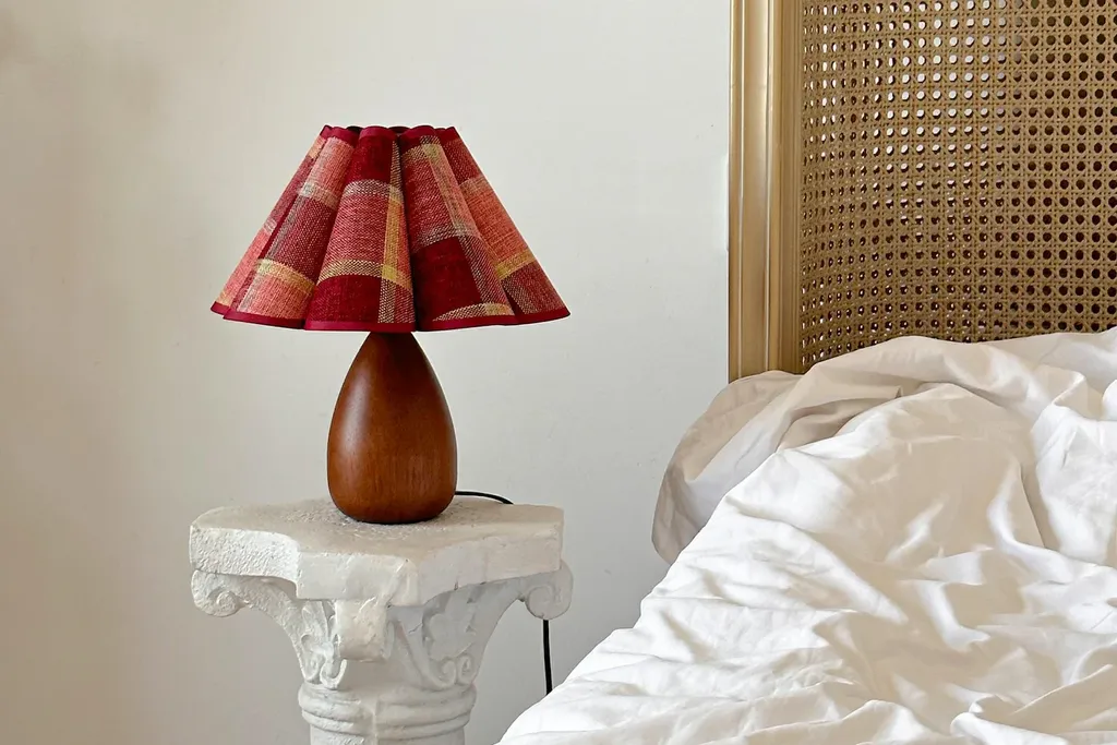 Bedside lamps with small plaid lampshades on tables beside a bed