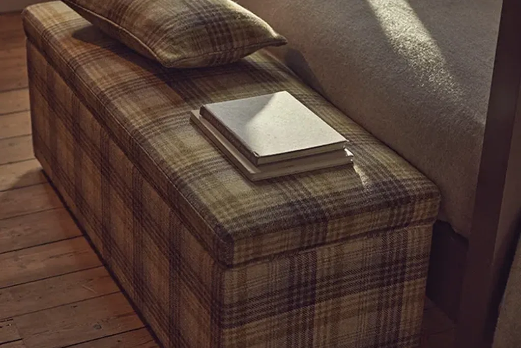Plaid upholstered bench at the foot of a bed with a folded quilt on it