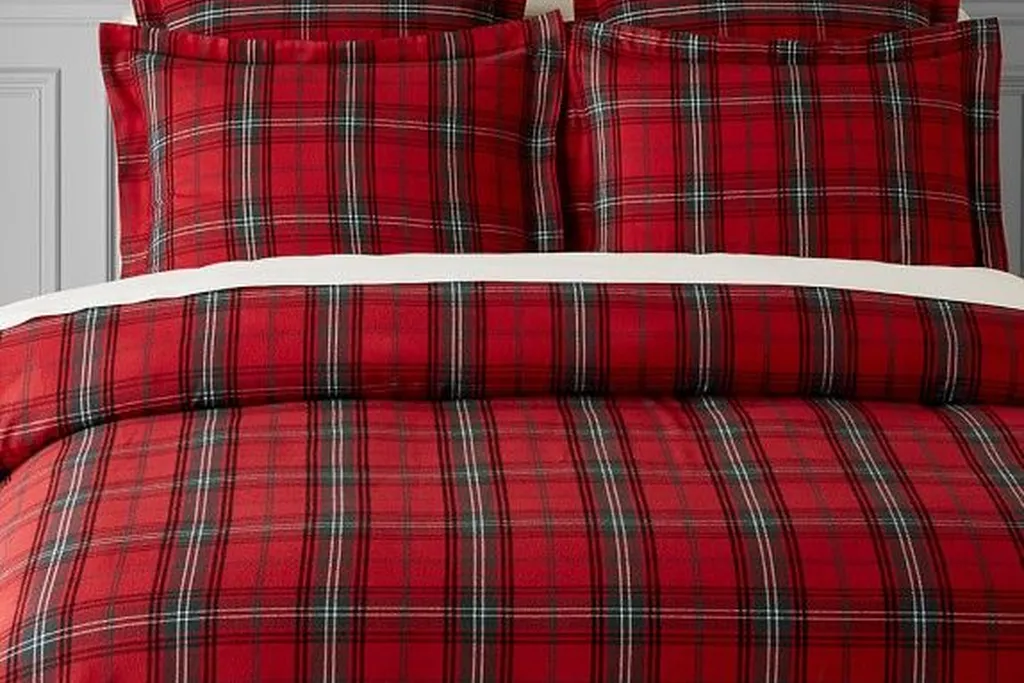Neutral bed layered with red tartan pillow covers and a throw for winter