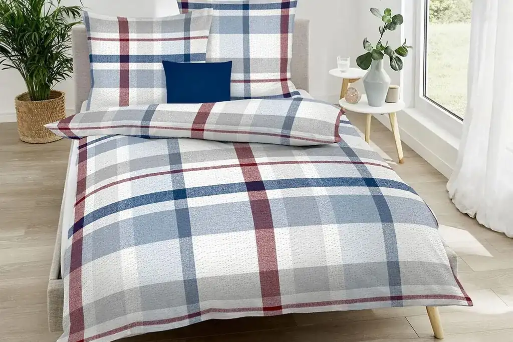 Light madras plaid coverlet in blue and pale coral on a summer bed