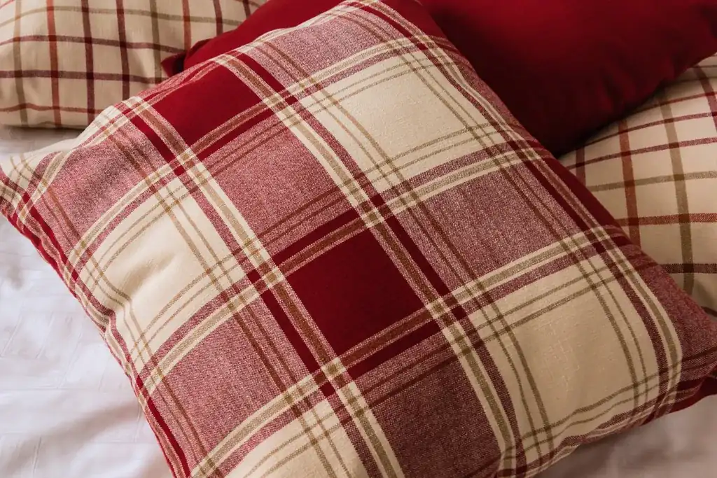 Plaid pillows separated by a solid lumbar cushion on a neatly made bed
