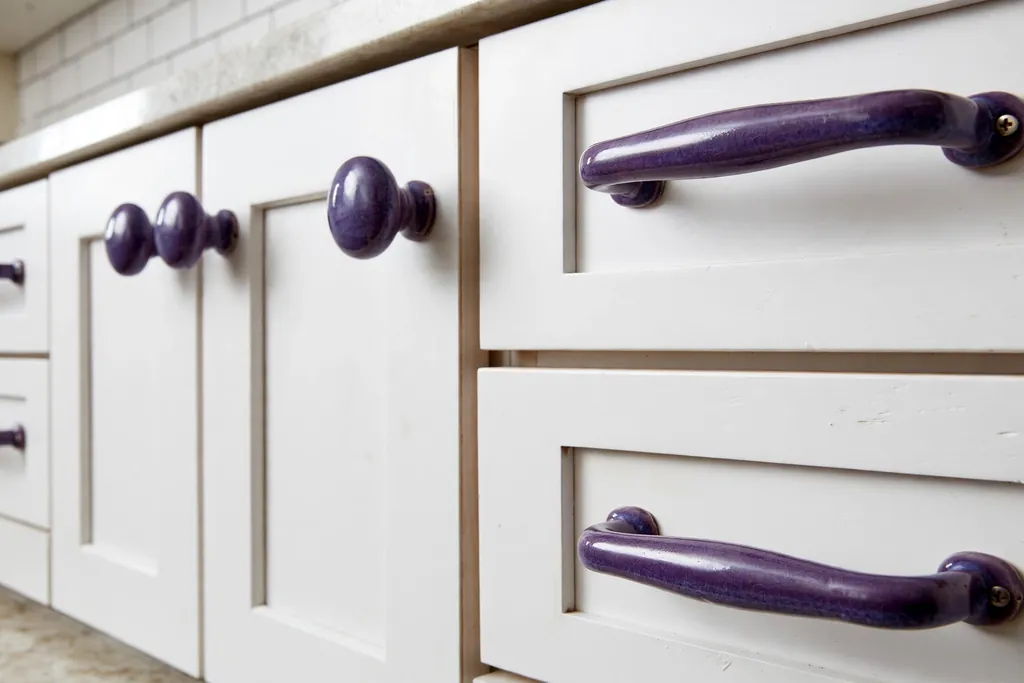 Close view of kitchen cabinets with purple ceramic knobs and pulls.