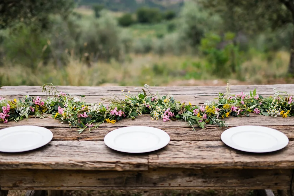 Bare wood table with a loose wildflower garland in pink, white, and yellow.