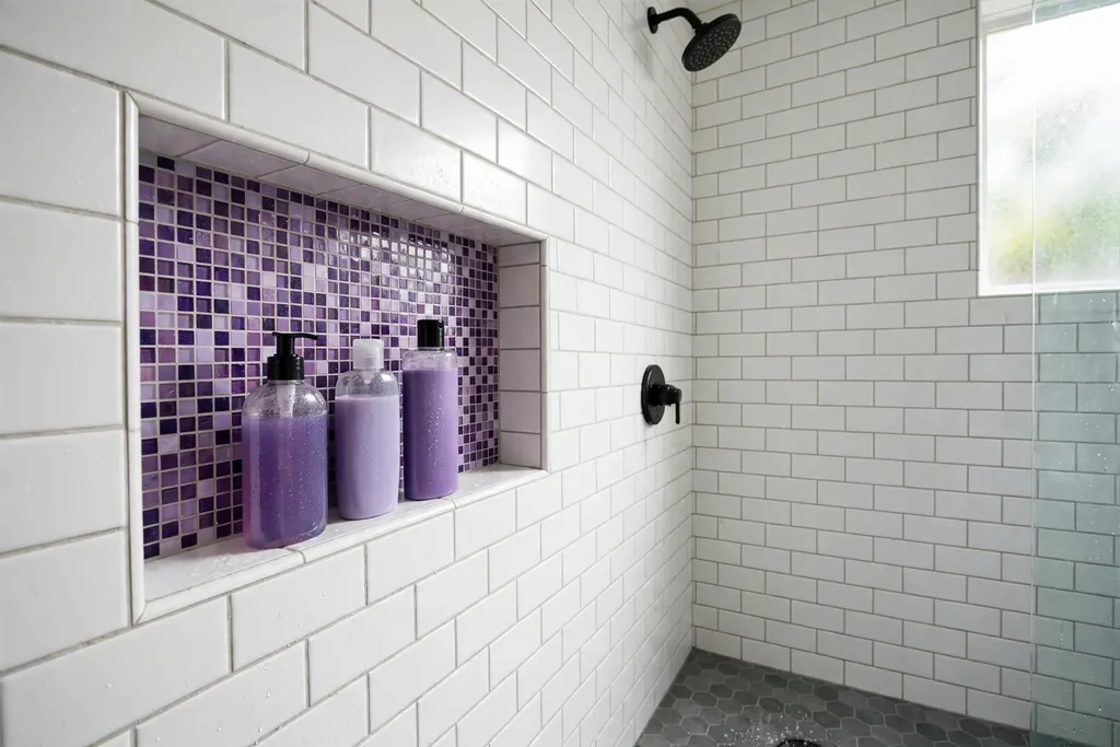 Shower niche lined with mixed purple mosaic tiles holding bottles.