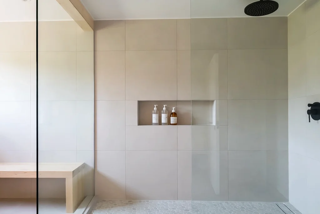 Walk-in shower with a glass panel, pale tiles, and a recessed niche in a Swedish bathroom.