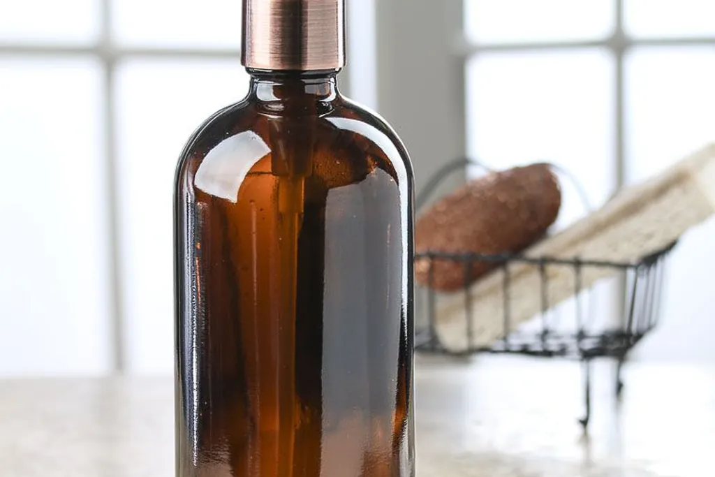 Amber glass soap dispenser with a pump on a kitchen counter near a window.