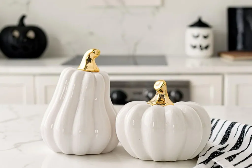 White ceramic pumpkins with gold stems on a marble kitchen counter.