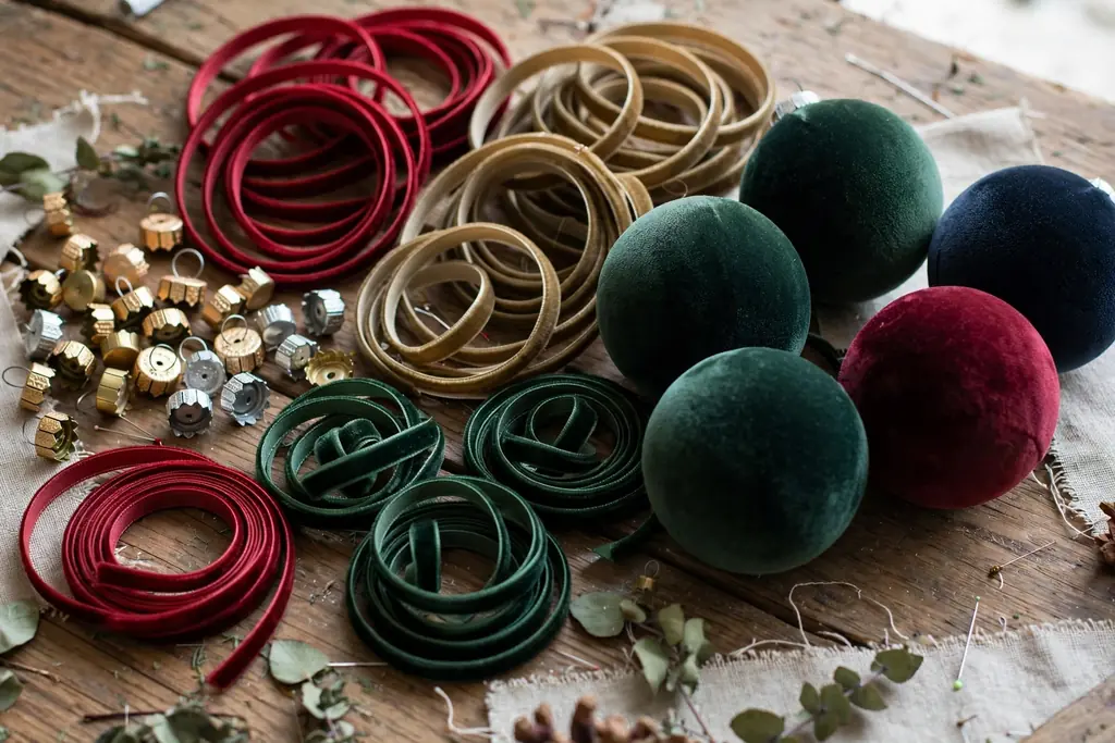 Ribbon loops and ornament caps beside velvet covered baubles on a table.