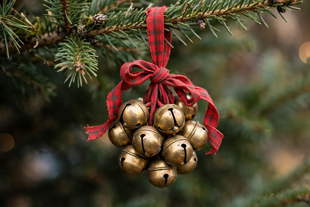 Cluster of small brass bells tied with ribbon hanging on a Christmas tree branch.