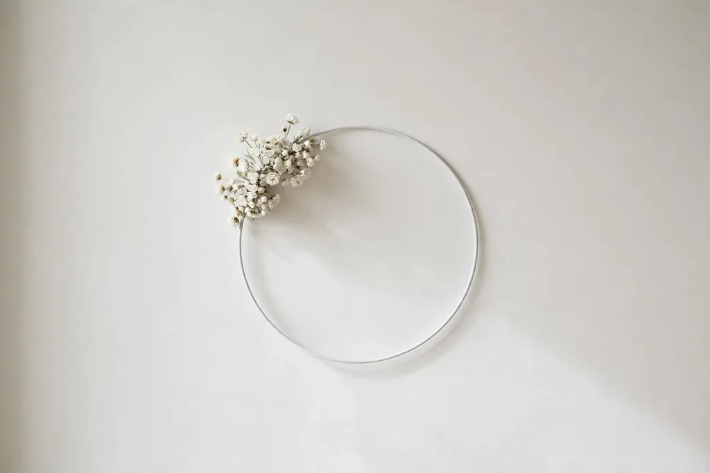 Minimal white hoop wreath with a small white flower cluster on a plain modern wall.