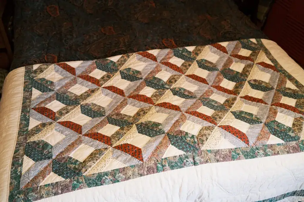 Quilt folded across the middle of a bed with plain bedding.