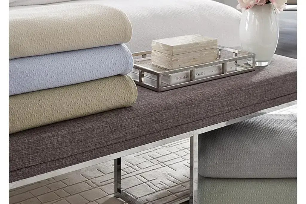 Bench with folded blankets at the foot of a bed.