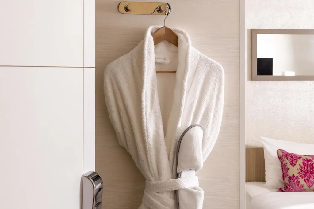 Robe on hooks near a bed with slippers below.