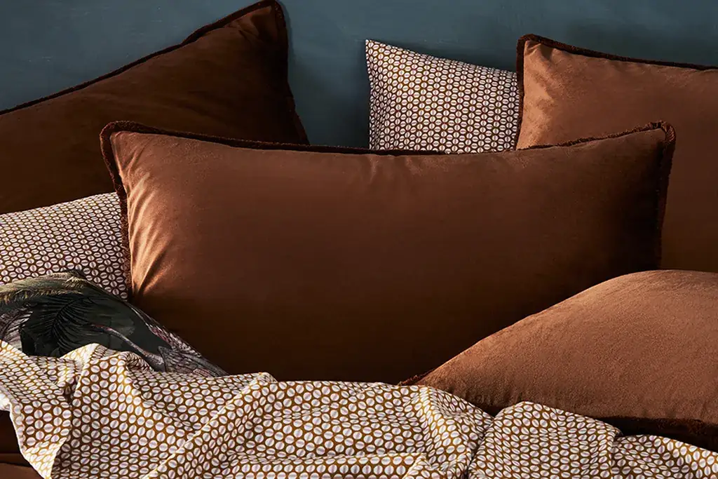 Neutral bed with warm colored pillow covers and a print above it.